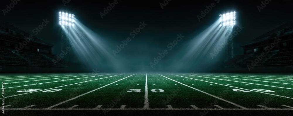 Fototapeta premium A brightly lit American football field at night with stadium lights shining down on the 50-yard line.