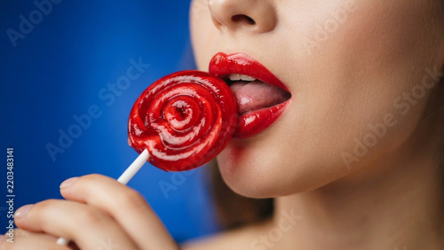 Woman with red lips eating a sweet round lollipop