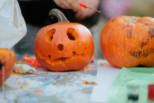 Carving Halloween Pumpkins At A Creative Workshop Table Close Up. Close up of a hand carving spooky jack o lantern face into an orange pumpkin