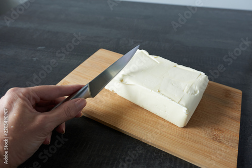 A woman's hands are cutting a piece of butter on a wooden board.