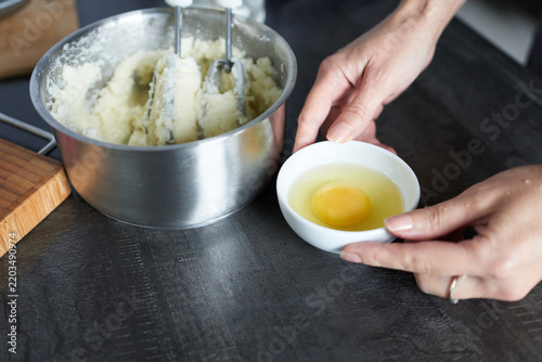 Hands of a young woman preparing dough in a metal bowl using a mixer. The process of preparing dough. Mixing ingredients.