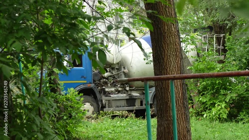 Blue concrete mixer truck driving through green foliage