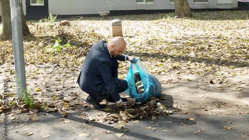 Businessman in a suit cleaning autumn leaves in a park