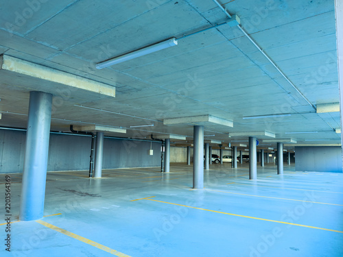 Parking area seen during daytime shows empty spaces with concrete pillars and blue walls