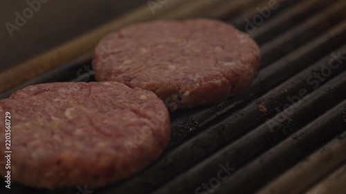 Raw beef burger patty placed on a hot restaurant grill, close-up of hamburger meat beginning to cook in a professional kitchen.