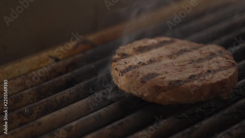 Juicy beef burger patty sizzling on a restaurant grill with dark sear marks, close-up of professional hamburger cooking.
