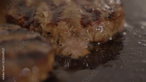 Juicy beef burger patty sizzling on a restaurant grill with dark sear marks, close-up of professional hamburger cooking.
