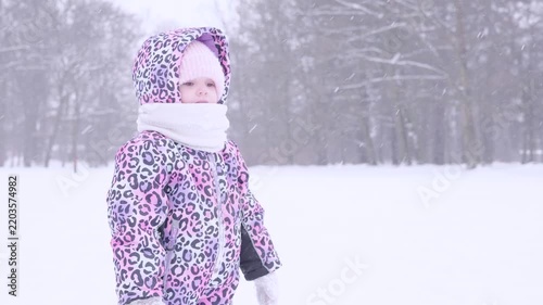 Child winter snow. Toddler shaking snow off mittens outdoors.