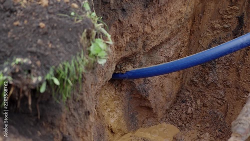 Thin blue plastic pipe hidden inside ground at construction site closeup. Plumbing utilities repair with modern supplies outdoors