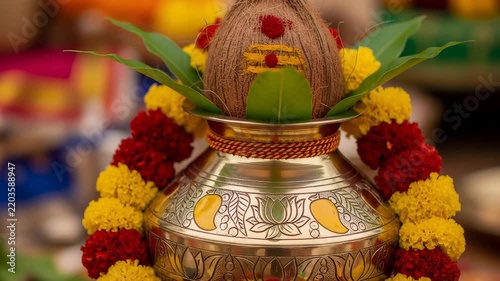 Traditional brass kalash used for Indian festival rituals. Holy coconut decorated with vermilion on metal pot adorned with marigold flower garland for Dussehra.