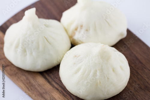 Obraz na plátně Three plump white steamed buns with pleated tops rest on a dark wooden cutting board