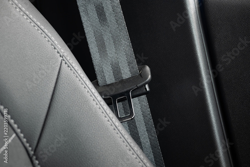 Car seat belt safety strap and metal latch tongue next to black leather upholstered seat inside modern vehicle