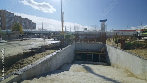 Concrete stairs lead into underground passage at active construction site. Bright sunlight illuminates urban modern development project