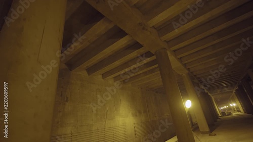 Row of thick concrete pillars supporting heavy ribbed ceiling. Dimly lit subterranean room highlights raw architectural foundation