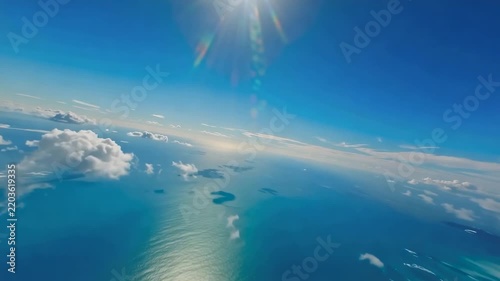Aerial view gliding above turquoise ocean waters and scattered white clouds beneath bright sunlight, expansive blue horizon and atmospheric seascape filmed from high altitude