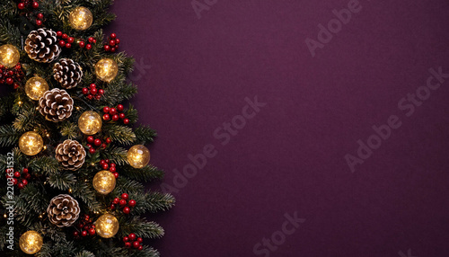 Christmas fir tree branch with pine cones and glowing lights on purple background