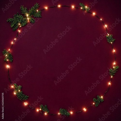 Christmas wreath made of fairy lights and fir branches on a dark red background
