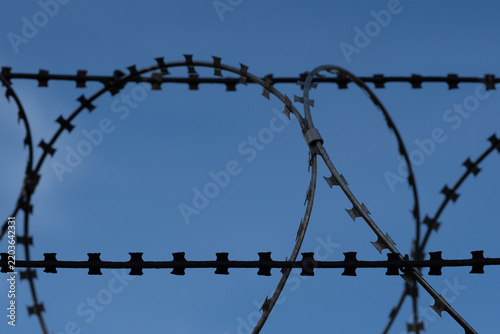 Foto Close-Up of nato barb wire roll on a fence with blue sky and light clouds in the