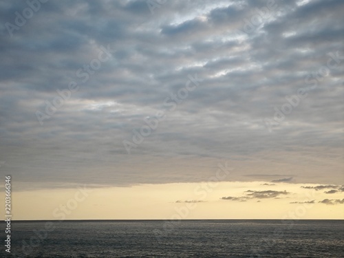 Overcast grey sky over the dark ocean at dusk. Seascape with a narrow band of yellow light at the horizon