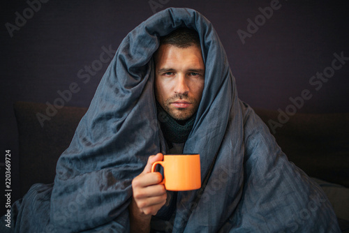 Bild auf Leinwand Picture of young man sits on bed and covered up with dark blue blanket
