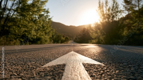 White arrow on an asphalt road pointing directly into a vibrant sunset over a scenic mountain landscape. Represents future direction, journey, and progress.
