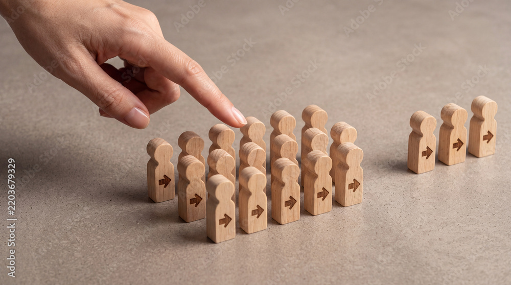 Obraz premium Close-up of a hand selecting a wooden figure from a crowd, symbolizing human resources, recruitment, leadership selection, talent management, and career choice in a professional business environment.