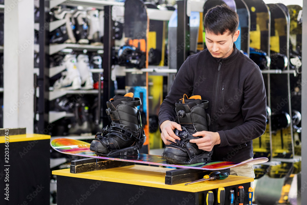 Obraz premium Snowboard boot Fitter or Ski Instructor adjusting Snowboard Boot and Binding, Preparing Equipment for Snowboarding on Winter Ski Resort. Snowboard Rental Equipment and Fitting service at Ski Resort.