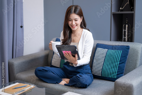 Young woman sitting on couch using tablet at home, relaxed lifestyle, smiling