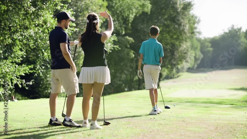 Family spending a sunny day at the golf course. A young boy practices his swing while his parents cheer him on from behind
