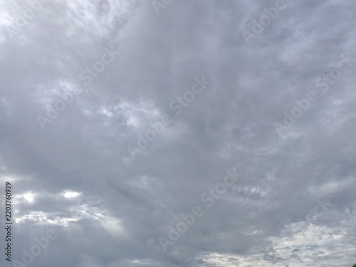 Dramatic overcast gray sky with soft sunlight breaking through thick clouds, creating a dramatic atmosphere ideal for backgrounds and nature concepts.