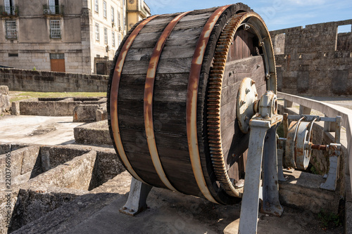 Vintage wooden industrial drum wheel with gears on stone ground.