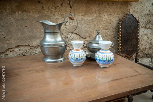 Antique pewter jug and ceramic vases on a wooden table.