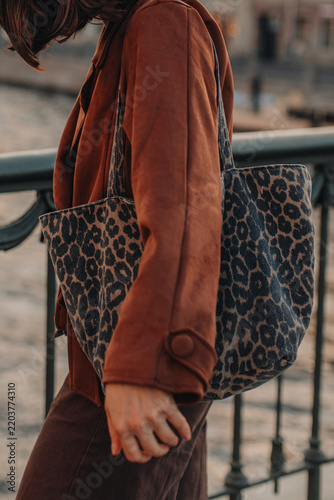 Obraz na plátně Trendy young woman wearing a brown suede jacket and carrying a leopard print bag