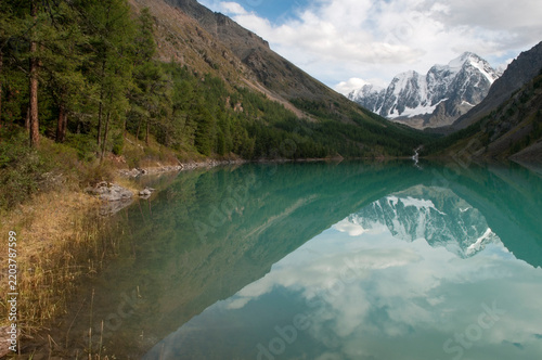Picturesque shoreline of the Lower Shavlinsky lake with mountain peaks named Dream, Fairy Tale and Beauty reflecting in the crystal-clear water, the Altai Republic, Russia
