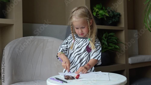 A cute little girl child sitting at a table and drawing or coloring on paper.