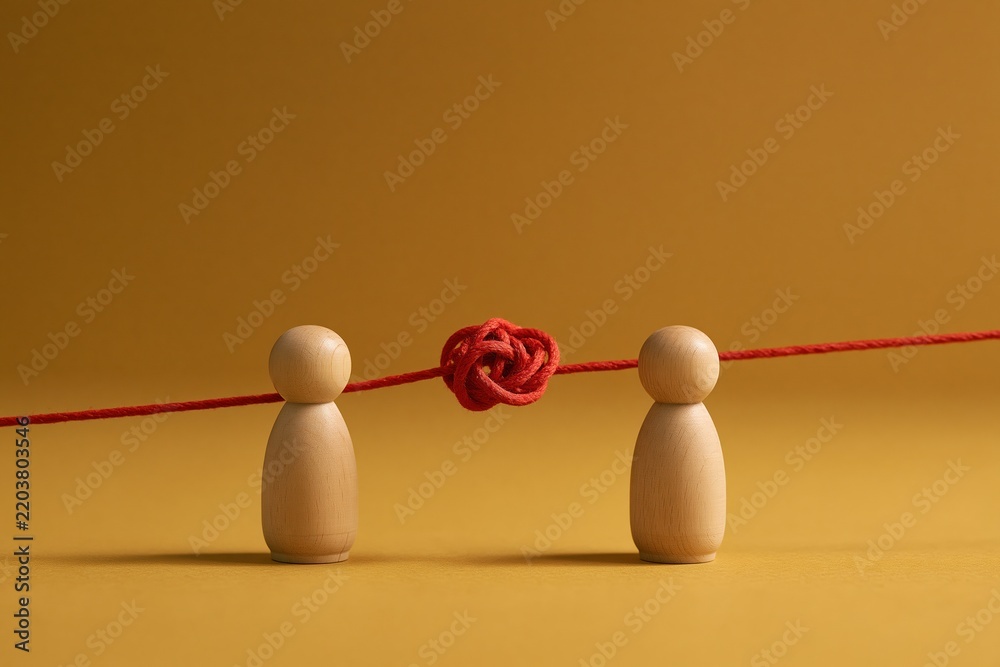 Obraz premium Two wooden figures face red knotted string on