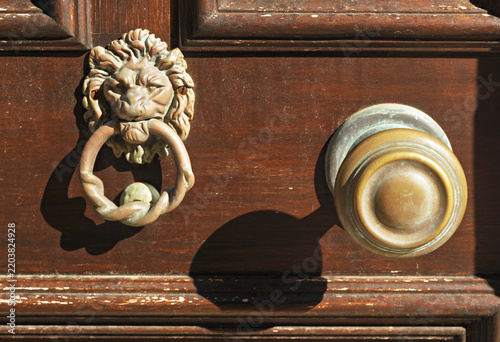 A Halki wooden door shows a dark lion knocker and round metal knob, their worn surface catching warm island light on rich brown grain.