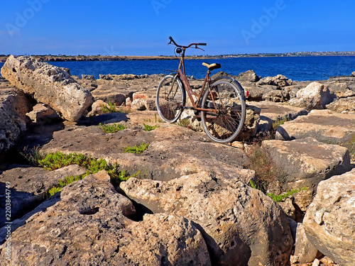 Bicicletta d'epoca parcheggiata sulle rocce della scogliera di Ognina con vista sul mare, Siracusa, Sicilia 641