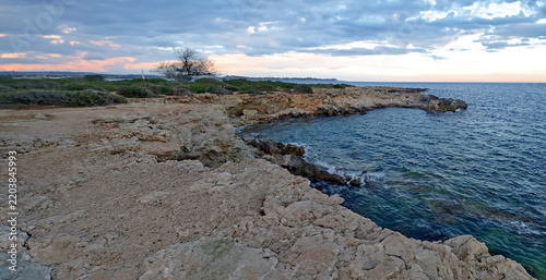 Illustrazione artistica di una costa rocciosa e baia al tramonto con cielo nuvoloso 692c93