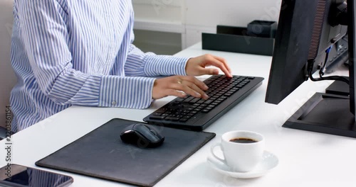 Professional typing on keyboard at office desk with coffee and smartphone nearby