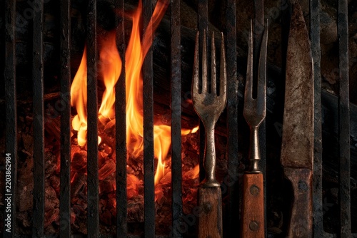 Vintage BBQ Utensils and Burning Charcoal Under a Rustic Iron Grill