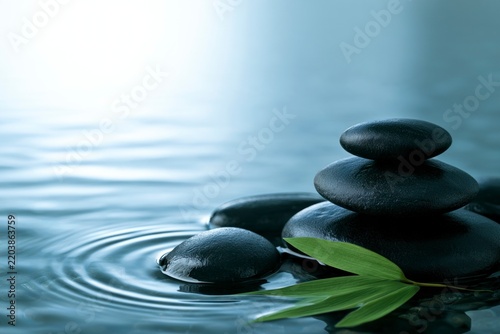 Zen stones balanced on calm water with green bamboo leaf, concept of meditation and relaxation