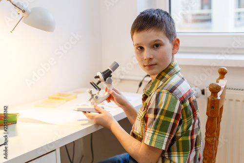 Schoolboy holding microscope during science lesson at home desk