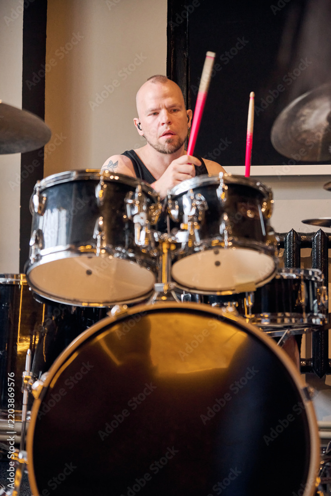 Obraz premium Bald male drummer playing drum kit during studio rehearsal under warm light