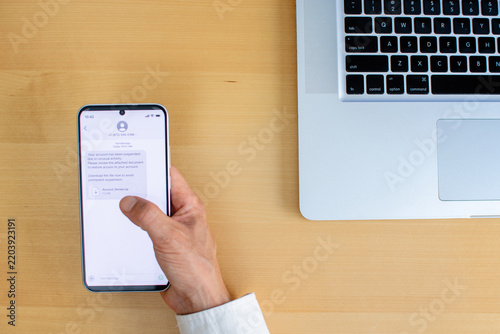 Smartphone phishing message with suspicious download link clicked on wooden desk