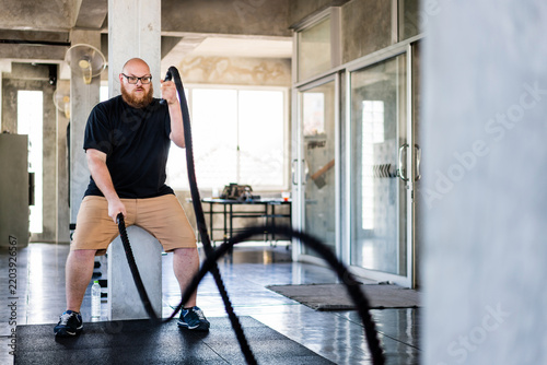 Cuadro en lienzo Man exercises with battle ropes in a modern gym, creating powerful rope waves during an intense workout session