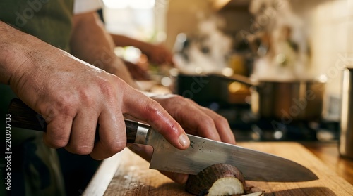 Professional Chef Hands Slicing Onion with Sharp Knife on Wooden Board in Commercial Kitchen