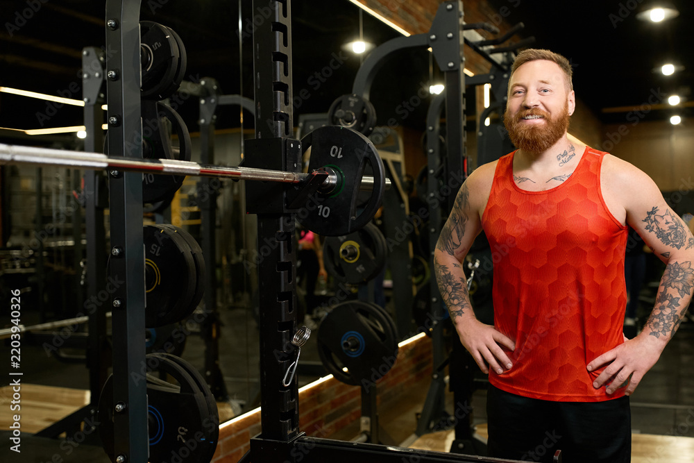 Obraz premium Handsome young man smiles confidently at modern gym while dressed in comfy sportswear