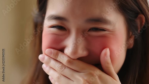 Young woman laughs softly, cheeks flushed with joy. She covers her mouth with her hand, eyes crinkled in delight. Her smile hides a moment of pure, spontaneous amusement