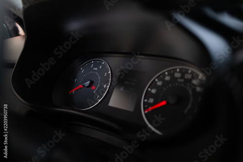 Close up view of a modern automobile instrument panel with illuminated dials and digital display in the dark. Vehicle interior details with speedometer, tachometer, and cockpit elements. Performance